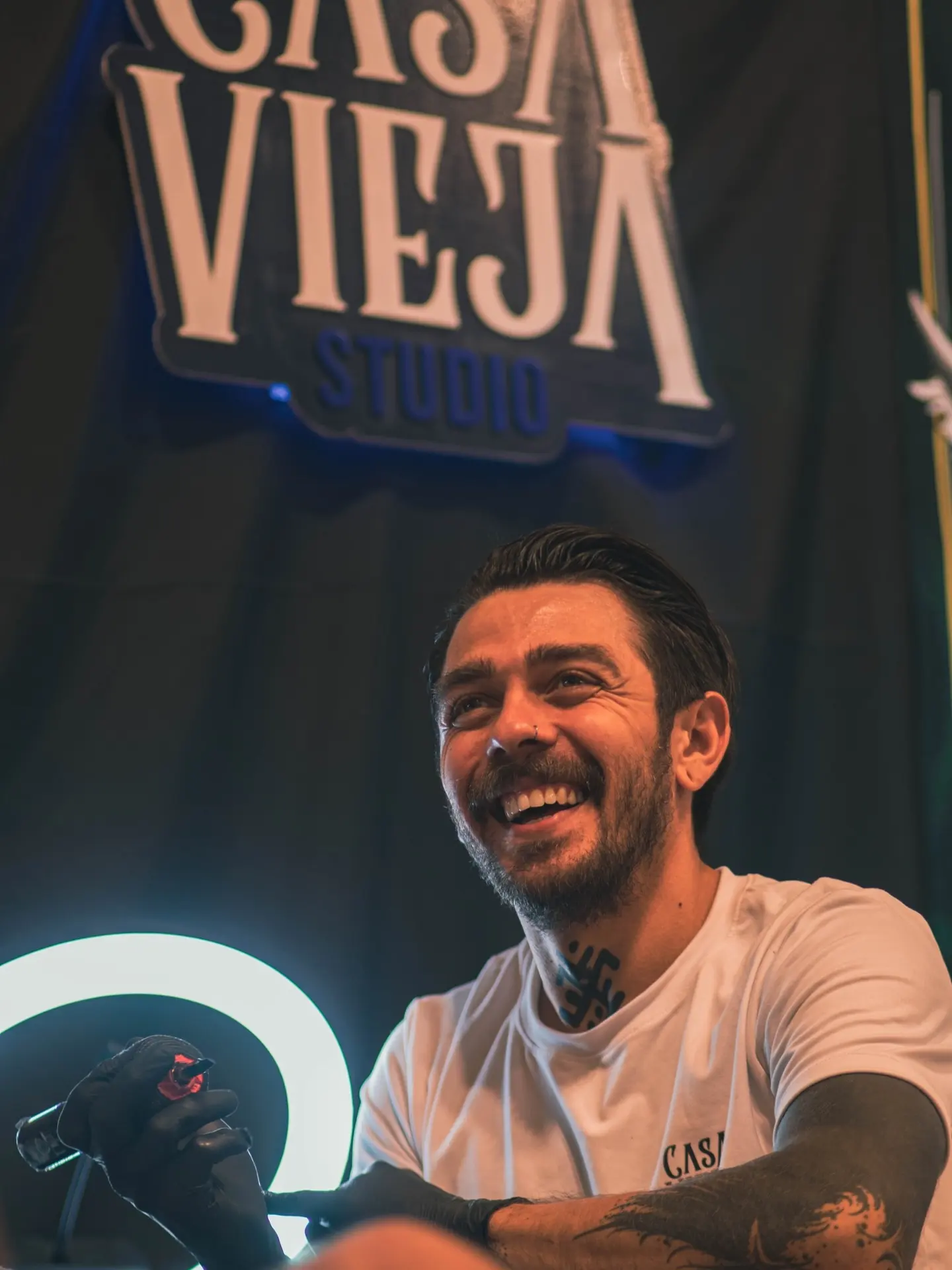 Maikol Araya sonriendo mientras tatúa bajo el letrero de Casa Vieja Studio